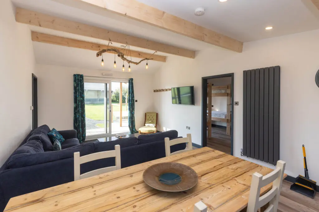 Bright and airy lounge area inside a holiday lodge at Little Pig Wellness near Bude, with blue sofa, wooden dining table and countryside views