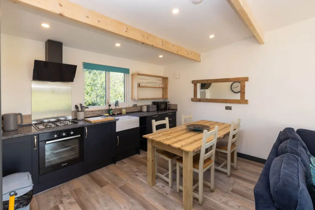Open plan kitchen and dining area inside a holiday lodge at Little Pig Wellness near Bude, Cornwall, with wooden flooring and teal accents
