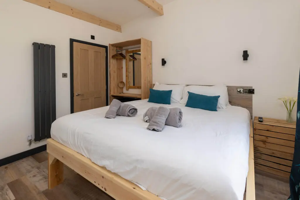 Bright double bedroom with teal soft furnishings inside a holiday lodge at Little Pig Wellness, near Bude, North Cornwall