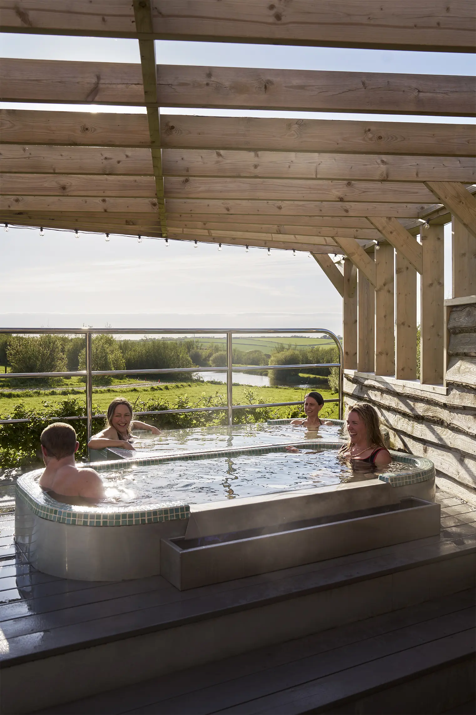 Colleagues relaxing together in an outdoor hot tub overlooking the North Cornwall countryside during a corporate wellness day at Little Pig Wellness.